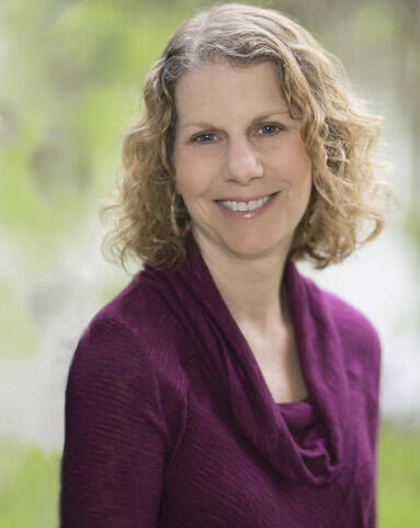 Photo of therapist Debbie Miller, standing outdoors, wearing a purple sweater, smiling.