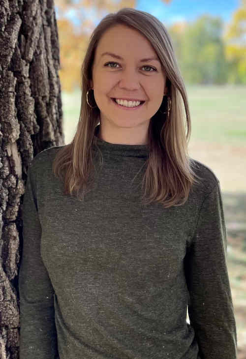 Photo of therapist, Jasmine Nix, standing outside beside a tree, wearing a green sweater, smiling.